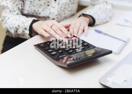 A woman considers on a calculator costs, revenues, expenses. Distribution of the family budget. Businesswomen is engaged in accounting. Stock Photo