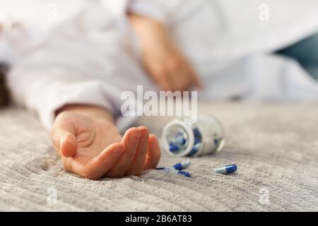 Woman’s hand close up committing suicide by overdosing on medication, pills and bottle beside. Overdose pills and addict concept background Stock Photo