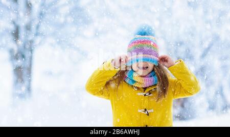 Child in knitted hat playing in snow on Christmas vacation. Winter outdoor fun. Knitting and outerwear for family. Kids play in snowy park. Little gir Stock Photo