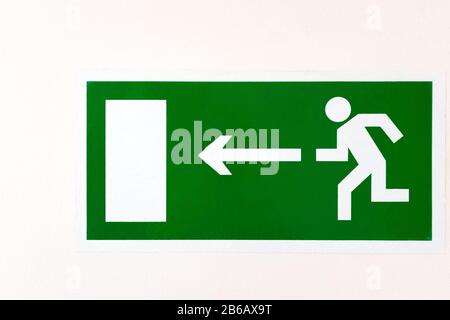 A green poster on a light wall. DIRECTION TO EVACUATION EXIT LEFT. Stock Photo