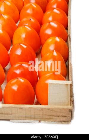 Persimmon fruit in the wooden box isolated on white. Clipping Path included. Juicy ripe persimmon in a large wooden box on a white background. Half wo Stock Photo