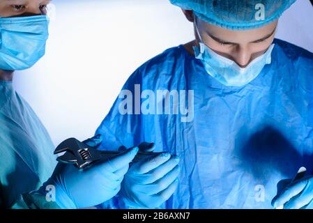close-up, portrait of two surgeons, in medical masks and a sterile gown. the assistant passes the wrench to the surgeon. Medical humor. Surgical joke. Stock Photo