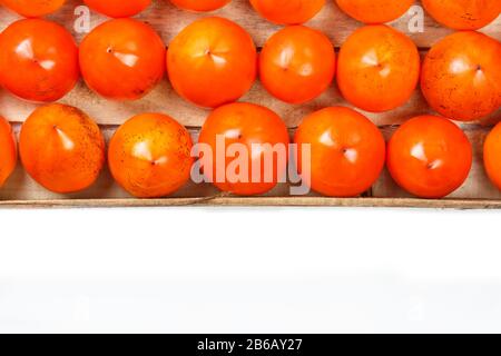 Persimmon fruit in the wooden box isolated on white. Clipping Path included. Juicy ripe persimmon in a large wooden box on a white background. The edg Stock Photo