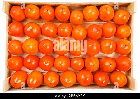Persimmon fruit in the wooden box isolated on white. Clipping Path included. Juicy ripe persimmon in a large wooden box on a white background. Stock Photo