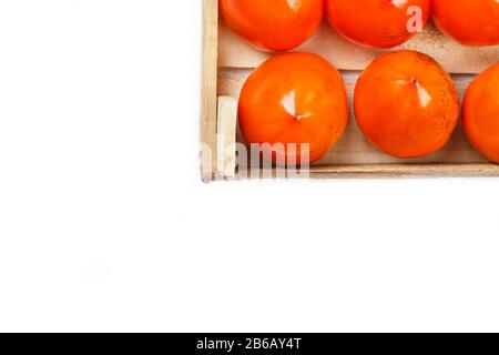 Persimmon fruit in the wooden box isolated on white. Clipping Path included. Juicy ripe persimmon in a large wooden box on a white background. The edg Stock Photo