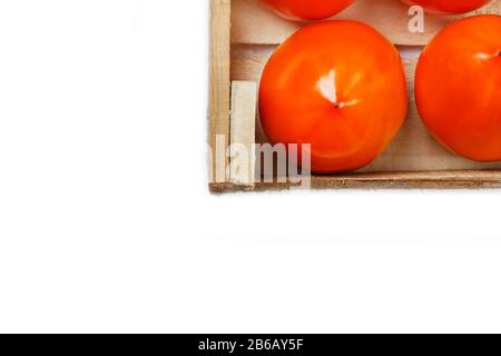 Persimmon fruit in the wooden box isolated on white. Clipping Path included. Juicy ripe persimmon in a large wooden box on a white background. The edg Stock Photo
