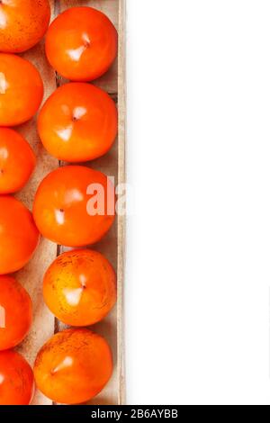 Persimmon fruit in the wooden box isolated on white. Clipping Path included. Juicy ripe persimmon in a large wooden box on a white background. The edg Stock Photo
