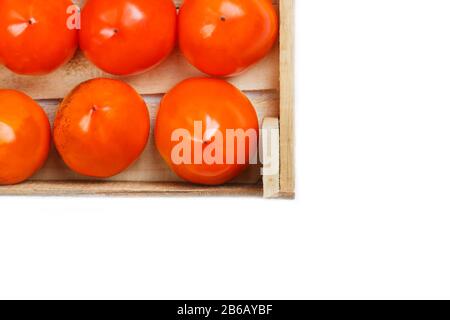 Persimmon fruit in the wooden box isolated on white. Clipping Path included. Juicy ripe persimmon in a large wooden box on a white background. The edg Stock Photo