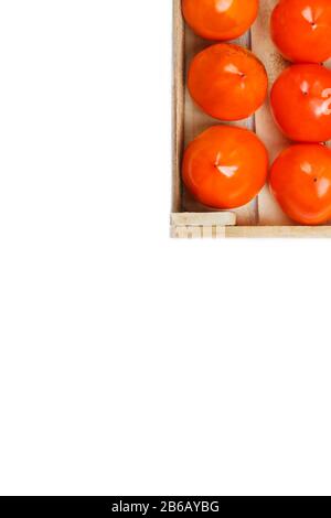 Persimmon fruit in the wooden box isolated on white. Clipping Path included. Juicy ripe persimmon in a large wooden box on a white background. The edg Stock Photo