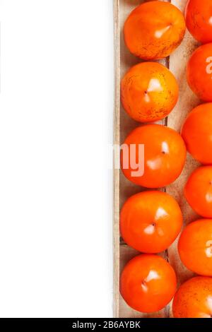 Persimmon fruit in the wooden box isolated on white. Clipping Path included. Juicy ripe persimmon in a large wooden box on a white background. The edg Stock Photo