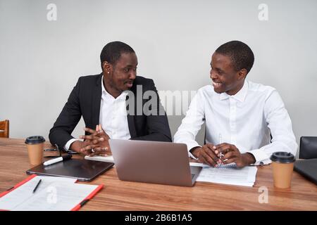 Laughing African American businessmen discussing paperwork with a coworker at a table in an office Stock Photo