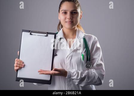 close-up, modal woman, doctor in a white coat and with a phonendoscope. holding a medical folder in his hand with a blank sheet, copy space. Studio ph Stock Photo