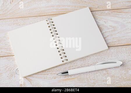 Opened spring notepad and white ballpoint pen on a white wooden textured surface. Business, education, keep diary and write notes concept. Copy space. Stock Photo