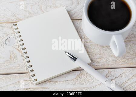 Opened spring notepad, white ballpoint pen and cup of coffee on a white wooden textured surface. Business, education, keep a diary and write notes. Stock Photo