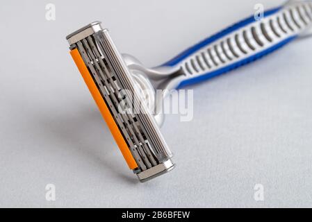 Close-up of new disposable shaving razor with triple blade on a pastel gray background. Silver blue plastic razor with orange lubricat strip. Stock Photo
