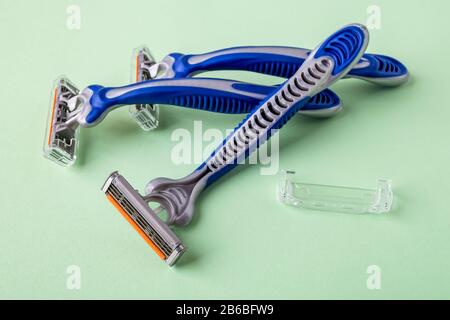 Three new disposable shaving razors with triple blade on a pastel green background. Silver blue plastic razor with orange lubricat strip. Stock Photo