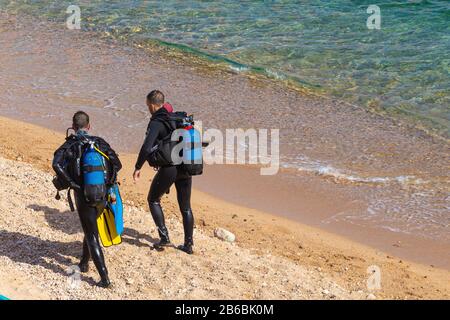 TOSSA DE MAR,SPAIN - AUGUST 4, 2019: Two unknown divers in wetsuits and scuba divers on a sandy beach near the water's edge are preparing for a dive Stock Photo