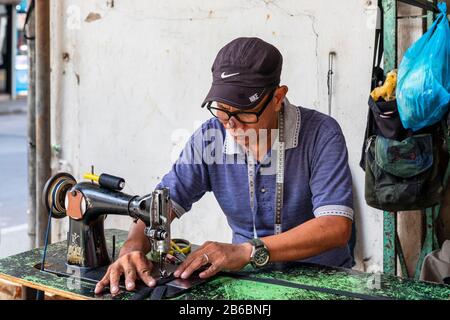 Local man making and repairing handbags and leather goods using an old sewing machine on the street in Sandakan city centre, Borneo, Sabah district, Stock Photo