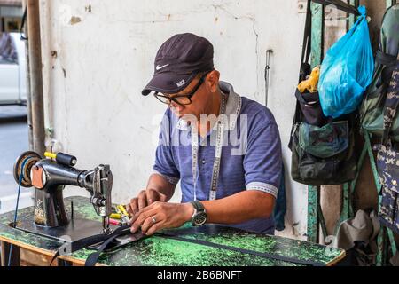 Local man making and repairing handbags and leather goods using an old sewing machine on the street in Sandakan city centre, Borneo, Sabah district, Stock Photo