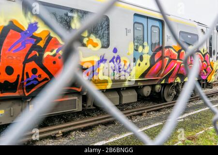 Graffiti on railway carriage seen though chain link fence. Stock Photo