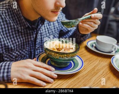 Man eating traditional asian soup from patterned wooden plate Stock Photo