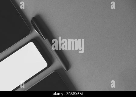 Business flat lay on dark paper background, monochrome image. Smartphone, tablet computer and notebook organizer on vintage background Stock Photo