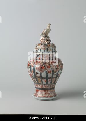 Baluster vase with cover to people in an interior rear grille, prunus trees and flower tendrils Balustervormige dekselpot van porselein met een spreidende voet, beschilderd in onderglazuur blauw en op het glazuur rood, zwart en goud. Op de wand twee keer twee mensen zittend in een interieur achter gemodelleerd en beschilderd traliewerk. Dit traliewerk is versierd met gemodelleerde en gedecoreerde prunusbomen en banden met bloemranken. Onder het traliewerk een band met bloemranken. Rond de voet een band met lotusranken. Op de hals drie cartouches met lotusranken. Imari. Manufacturer : pottenbak Stock Photo