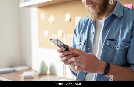 Close up view of young man standing at home office using smart phone mobile app. Stock Photo
