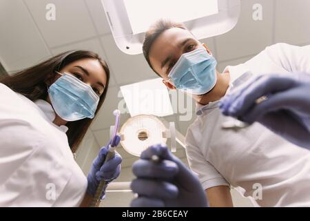 Dentist and assistant at a treatment, from the perspective of a patient. Dentist Holding Dental Tools. Stock Photo