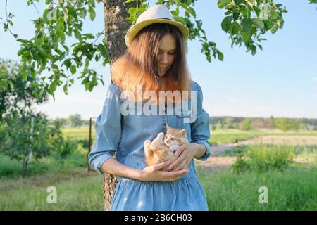 Teenager girl in hat denim dress holding little ginger kitten in hands Stock Photo