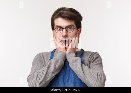 Close-up portrait shocked and speechless young male employee gossiping about coworker, hear stunning unbelievable news, hold hands on face, staring Stock Photo