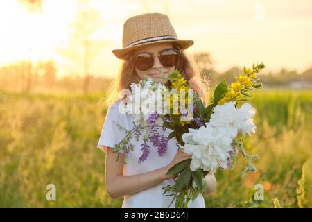 Portrait of child girl in hat sunglasses with flowers in meadow Stock Photo