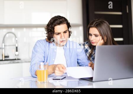 Content young couple examining papers while filing income tax returns in cozy kitchen Stock Photo