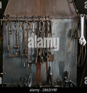 rough iron vintage blacksmith and locksmith tools hung on the metal wall of the forge furnace Stock Photo