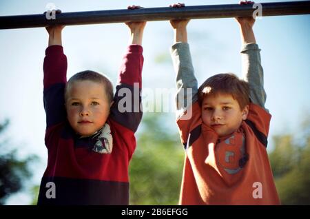 Two boys hanging on monkey bars Stock Photo