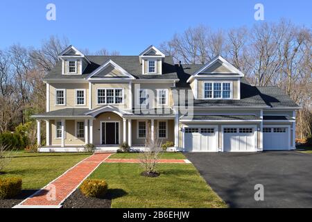 New house, colonial style, frontal view. Brick entrance walkway, paved driveway, landscaped garden. Stock Photo