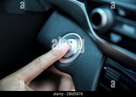 Hand pushing a car engine's Start and stop button Stock Photo