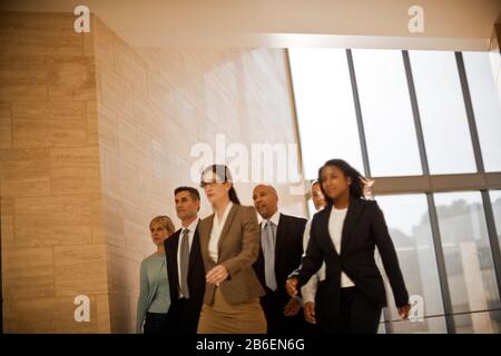 Group of businesswoman and businessmen striding with determination through their office hallway. Stock Photo