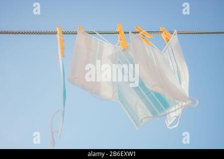 Medical face masks hanging on a clothesline with yellow clothespins in blue sky background. Stock Photo