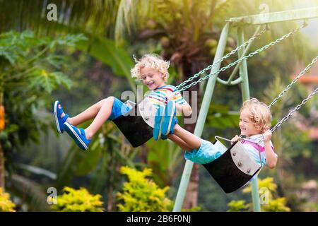 Child playing on outdoor playground. Kids play on school or kindergarten yard. Active kid on colorful swing. Healthy summer activity for children. Lit Stock Photo