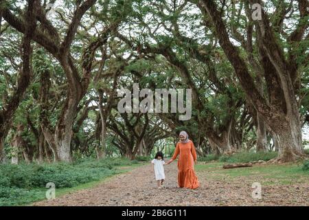 muslim mother hold hand with daugther walking in the forest between large trees Stock Photo