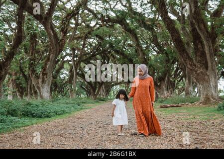 muslim mother hold hand with daugther walking in the forest between large trees Stock Photo