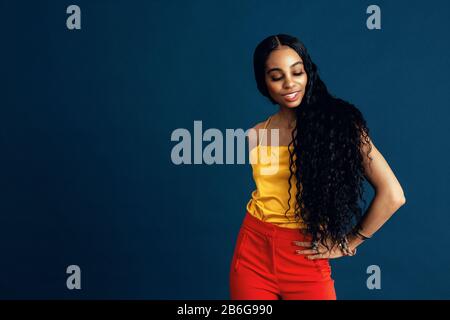 Portrait of a happy young woman with very long  beautiful black curly hair smiling and looking down, with one arm on waist Stock Photo