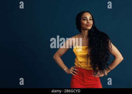 Portrait of a confident young woman with very long  beautiful black curly hair smiling with arms on waist Stock Photo