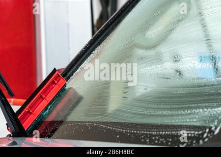 squeegee cleaning or washing a car windscreen, windshield with trails of soap bubbles on the surface of the glass Stock Photo
