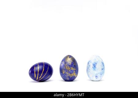 Three easter eggs trendy colored classic blue, white and golden decorated on white table. Happy Easter card with copy space for text. Minimal style Stock Photo