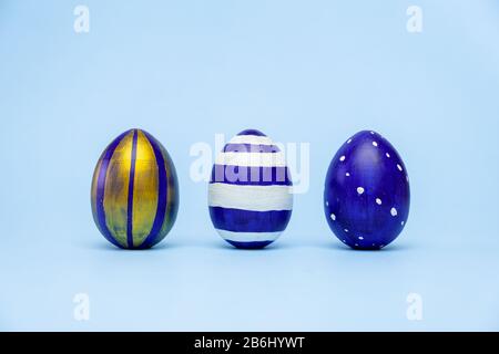 Three easter trendy colored classic blue and golden decorated eggs striped pattern on blue. Happy Easter card with copy space for text. Minimal style Stock Photo