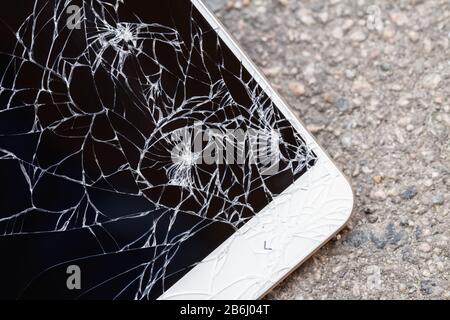 Smartphone with broken blue display screen is lying on the asphalt. Closeup, selective focus Stock Photo