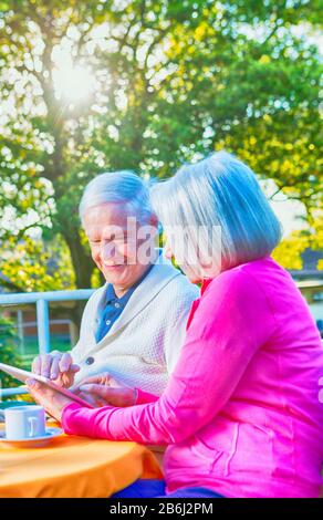 Happy retired couple using tablet relaxing outdoor. Stock Photo