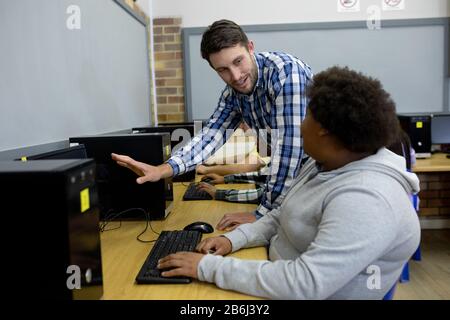 Side view of teacher helping student on computer Stock Photo